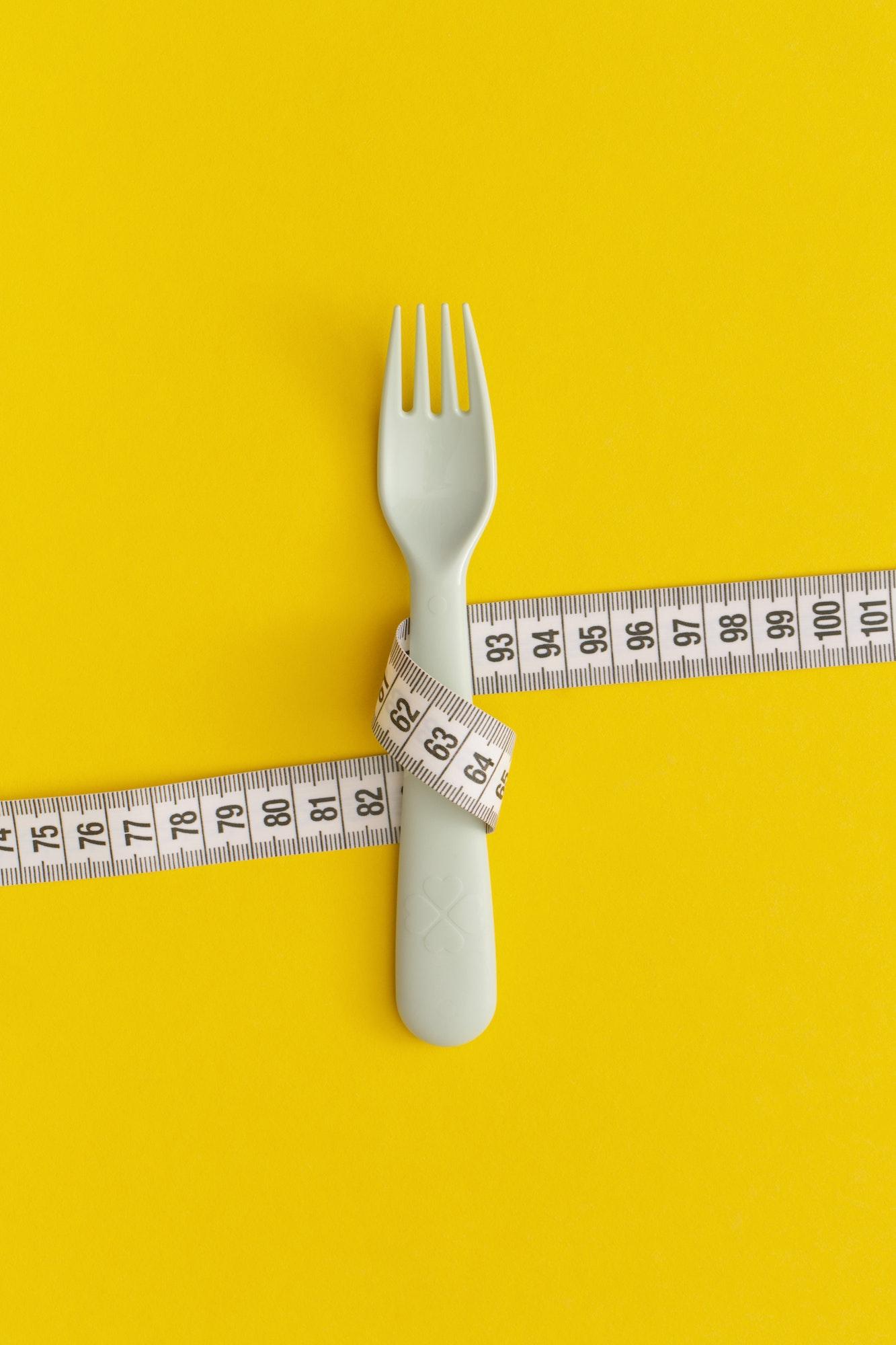 Measuring tape and fork on yellow background. Weight loss concept